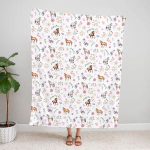 May include: White fabric with a repeating pattern of watercolour horses and flowers. The horses are brown and white and the flowers are pink, purple and yellow.