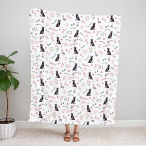 May include: White fleece blanket with a repeating pattern of black labrador retrievers, pink and green flowers, and the word "Harper" in pink.