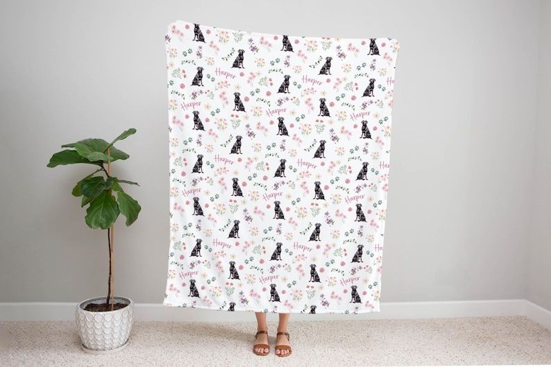 May include: White fleece blanket with a repeating pattern of black labrador retrievers, pink and green flowers, and the word "Harper" in pink.