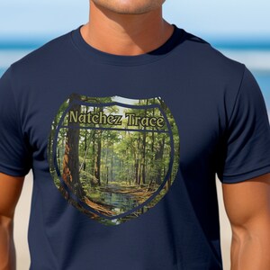 Op de afbeelding: Een marineblauw t-shirt met een ronde afbeelding van een bospaadje. De afbeelding bevat de tekst "Natchez Trace" in een gouden lettertype.