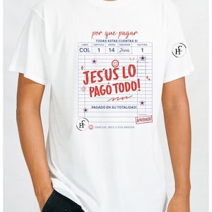 May include: White t-shirt with a graphic design. The design includes text in Spanish, a ledger-style layout, and the words "JESUS LO PAGÓ TODO!" in red. The shirt also features a small logo on the sleeve.