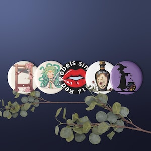 Puede incluir: Un conjunto de cinco botones redondos con varios diseños. Uno presenta una guillotina con detalles florales, otro a Medusa, y un tercero unos labios rojos con el texto "Rebels Sin 71". Los botones restantes muestran una botella de poción y una bruja.