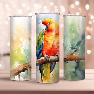 May include: Three stainless steel tumblers with a watercolor design of a parrot perched on a branch. The parrot is orange, yellow, green, and blue. The background is a watercolor wash of green, blue, and yellow.