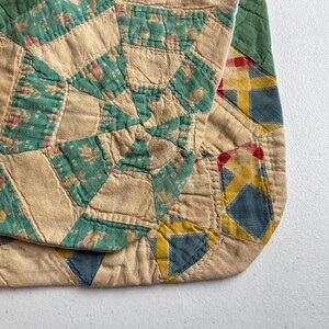 May include: A quilted textile featuring a patchwork design with cream-colored fabric and teal green sections patterned with small floral motifs. The piece includes geometric shapes in blue, yellow, and red, with visible stitching throughout the fabric.