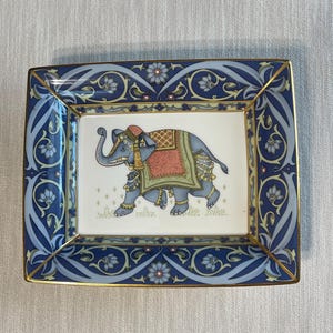 May include: A rectangular porcelain tray featuring a central illustration of a grey elephant adorned with a red and gold blanket and headpiece. The border displays a blue and light blue floral scroll pattern with gold trim on the edges.