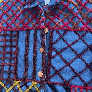 May include: Blue denim jacket with a patchwork design. The jacket features a variety of embroidered patterns in red, yellow, and brown, with wooden buttons down the front. The collar and cuffs are also detailed with embroidery.