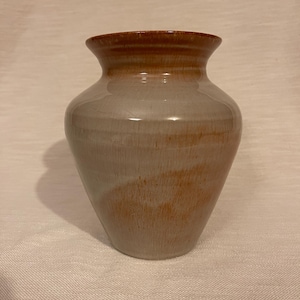 May include: A handmade ceramic vase with a wide base and a narrow neck. The vase has a light gray body with brown accents around the rim and on the lower portion. The vase is approximately 8 inches tall.
