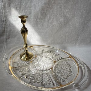May include: A clear glass serving tray with a gold rim and a decorative leaf pattern. A brass candlestick holder is placed on the tray. The tray is oval-shaped with three divided sections.