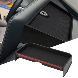 May include: Black car console tray with a textured surface and a red accent. The tray is designed to fit into a car's interior, providing additional storage space. The image shows the tray installed in a car.