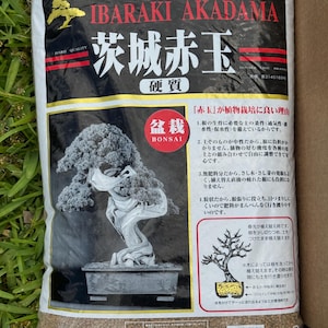 May include: A bag of Ibaraki Akadama bonsai soil. The bag is white with red and black text, including "Ibaraki Akadama" and Japanese characters. A bonsai tree illustration is on the bag, along with text in Japanese.