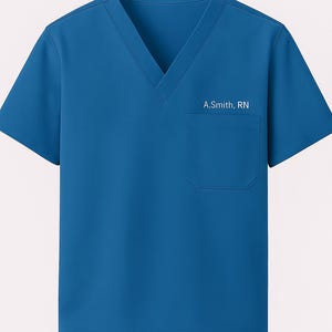 Pode incluir: Uma blusa azul com decote em V e bolso no peito. O texto "A.Smith, RN" está impresso no lado direito do peito. A blusa de manga curta é feita de um tecido liso.
