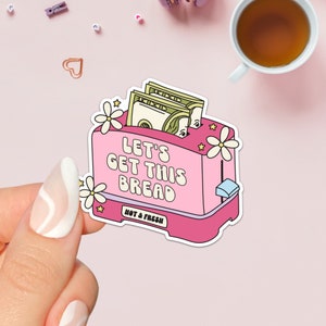 May include: Pink toaster with money inside, flowers on top, and the text "Let's Get This Bread" and "Hot & Fresh".