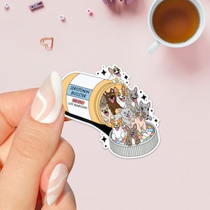 May include: A sticker featuring a cartoon pill bottle labeled "Serotonin Booster" with the side effect "Cute Aggression." The bottle is overflowing with various cartoon dogs. The sticker is held by a hand with a light pink and white nail design.