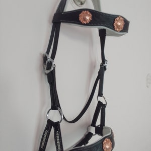 May include: Black leather horse bridle with decorative copper-colored floral accents. The bridle features silver-colored metal hardware and white padding. The design includes embossed floral patterns and rhinestone detailing.