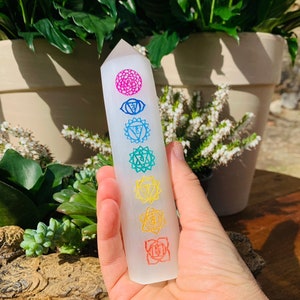 以下が含まれることがあります： 虹色のチャクラシンボルが7つ刻まれた白いセレナイトクリスタルワンド。シンボルは、クラウンチャクラからルートチャクラの順に並んでいます。