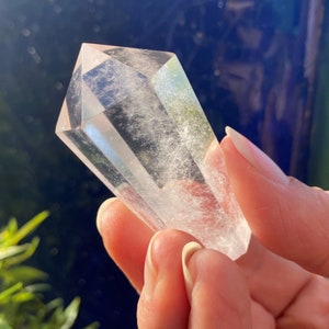 May include: A clear quartz crystal point with a double terminated shape. The crystal is smooth and polished, with a slight cloudy appearance.