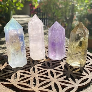 May include: Four crystal points in various colors, including iridescent, pink, purple, and yellow, are arranged on a wooden base with a geometric design.