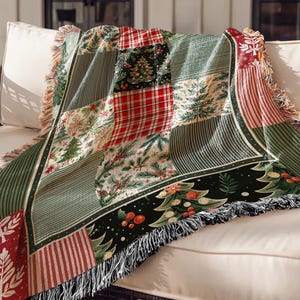 May include: A patchwork Christmas-themed throw blanket with a variety of patterns. The blanket features squares of red plaid, green stripes, and Christmas tree designs. The edges are fringed with a neutral color.