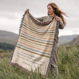 May include: A woven throw blanket featuring horizontal stripes in muted tones of blue, tan, and pink. The blanket displays the text: For I know the plans I have for you, declares the Lord, plans to prosper you and not harm you, plans to give you hope and a future. Jeremiah 29:11.