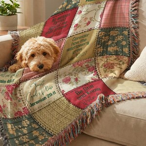 May include: A woven throw blanket featuring a patchwork design of floral patterns and solid squares with printed religious text including "No weapon formed against me shall prosper," "Trust God's Plan," and "Be Still and Know." A small golden dog rests on it.