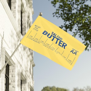 Puede incluir: Una bandera amarilla con las palabras "SALTED BUTTER" en azul. La bandera también incluye marcas de medición para cucharadas y tazas, y el texto "NET WT. 4 OZ. (113 g)" y "GRADE AA".