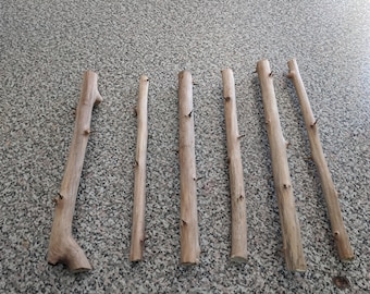 May include: Seven wooden sticks with sharp points at the ends. The sticks are arranged horizontally on a gray speckled surface.