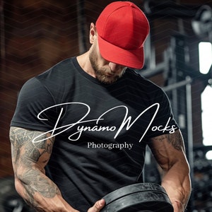 May include: A man wearing a black t-shirt with the text "Dynamo Mocks Photography" and a red baseball cap is lifting a black weight plate. He has tattoos on his arms.