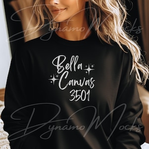 May include: Black crew neck sweatshirt with the text "Bella Canvas 3501" in a white script font. The sweatshirt is a solid black color and appears to be made of a soft material. The text is centered on the front of the shirt.