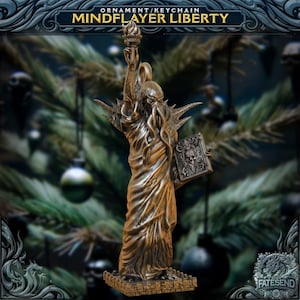 May include: A bronze-colored ornament or keychain featuring a statue of Liberty with a Cthulhu-like head, holding a torch and a book. The text "MINDPLAYER LIBERTY" is at the top. The ornament is on display in front of a Christmas tree.