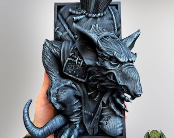 May include: A detailed, dark gray sculpture of a rat-like creature with a basket on its back. The sculpture has intricate details, including fur, claws, and armor. The creature is set against a black rectangular frame.
