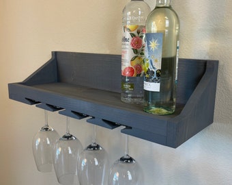 May include: A dark gray wooden wall-mounted wine rack with a shelf and four glass holders. Two bottles of alcohol are on the shelf, one is a clear bottle with a pink and white label that says "Malibu One Coconut Rum", the other is a clear bottle with a blue and white label.