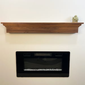 May include: A dark wood mantel shelf with a small green figurine on top. Below the shelf is a black electric fireplace with a realistic crystal-like fire effect.