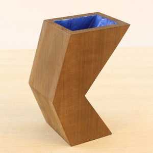 May include: A wooden vase with a blue interior. The vase is shaped like a geometric figure with a sharp angle.