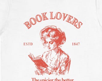 May include: White t-shirt with a red graphic. The graphic features the text "BOOK LOVERS" above an illustration of a woman reading a book. Below the illustration is the text "The spicier the better."