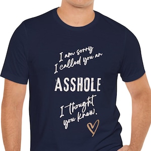May include: Navy blue t-shirt with white text: "I am sorry I called you an ASSHOLE I thought you knew." A gold heart is below the text. The shirt is worn by a person.