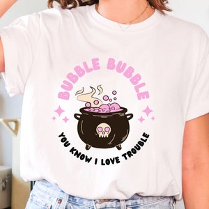 Puede incluir: Camiseta blanca con un gráfico rosa y negro de un caldero con burbujas y el texto "Bubble Bubble You Know I Love Trouble".