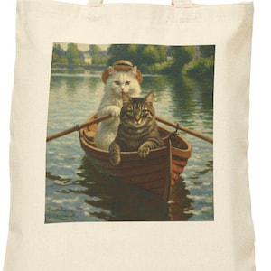 Puede incluir: Bolso tote de color crema con una pintura de dos gatos en una barca en un lago. Un gato lleva un sombrero y rema, mientras que el otro está sentado en la barca. El fondo muestra árboles y agua.