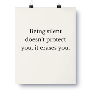 May include: A poster with the text "Being silent doesn't protect you, it erases you." The poster is cream-colored and held by two black binder clips. The text is in a simple, sans-serif font.