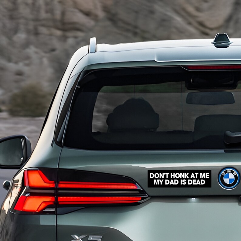 Peut inclure: Une voiture argent&eacute;e avec un autocollant noir sur le pare-chocs qui dit "Ne klaxonne pas, mon p&egrave;re est mort".