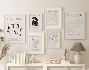 May include: A set of six digital art prints featuring black and white line drawings of dancers and faces. The prints are framed in white and have the text "Matisse" and "Picasso" on them. The prints are displayed on a white wall above a white dresser with a white lamp and a wicker basket.