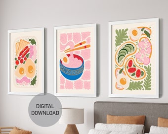 May include: Three digital prints of illustrations of breakfast foods. The prints are framed in white and feature a pink, green, and white color scheme. The prints are hung on a white wall above a bed with a brown blanket.