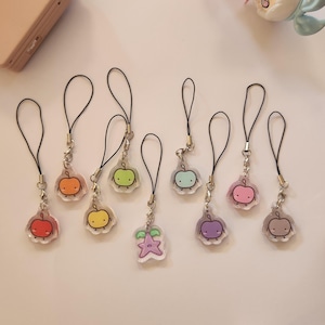 May include: A selection of fruit-shaped charms with black cords. Each charm features a different fruit design, including apples, lemons, and a star fruit, with cute cartoon faces. The charms are attached to silver-coloured metal clasps.