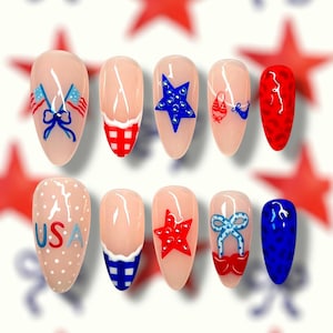 Puede incluir: Un conjunto de diez uñas artificiales con base nude, decoradas con diseños patrióticos. Los diseños incluyen banderas americanas, estrellas, lazos y las letras "USA" en rojo, blanco y azul. Las uñas tienen forma ovalada.