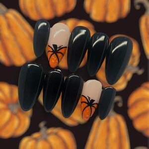 Puede incluir: Conjunto de diez uñas postizas negras en forma de almendra con un diseño de calabaza en dos de las uñas. Las calabazas son de color naranja con tallos negros y un contorno negro.