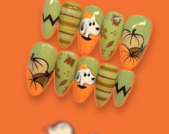 May include: Set of six green and orange false nails with a fall theme. The nails feature a cartoon dog, pumpkins, and leaves.