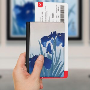May include: A passport holder featuring a blue iris floral print on a light background, containing a boarding pass for Maria Smith, flight F3954 to New York, seat 9A, boarding at 09:30. The holder has a solid black spine and a rectangular shape.
