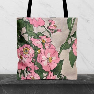 Peut inclure: Sac fourre-tout avec un motif floral de roses roses, de feuilles et de tiges vertes sur fond beige. Le sac a des poignées noires. Le motif floral est une illustration stylisée.