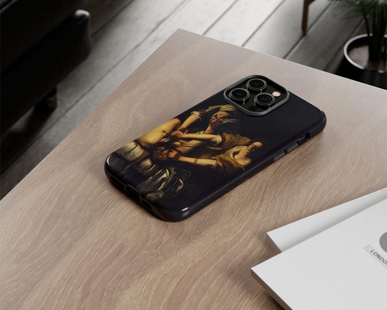 May include: Black iPhone case featuring a classical painting of figures in shades of brown, beige, and white. The case has a glossy finish and a camera cutout. The phone case is resting on a light brown wooden surface.