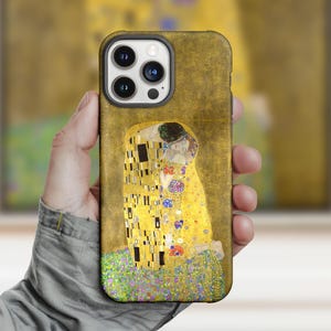 Może przedstawiać: Etui na telefon z grafiką "Pocałunek" Gustava Klimta. Etui ma złote tło z kultowym wizerunkiem obejmującej się pary. Projekt zawiera złote, żółte, czarne i kwiatowe akcenty, oferując klasyczną estetykę inspirowaną sztuką.