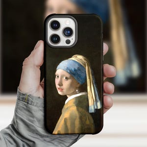 May include: Black phone case with a print of Johannes Vermeer's "Girl with a Pearl Earring". The case displays the subject's blue headscarf, pearl earring, and golden jacket. The phone case has a black border and a camera cutout.